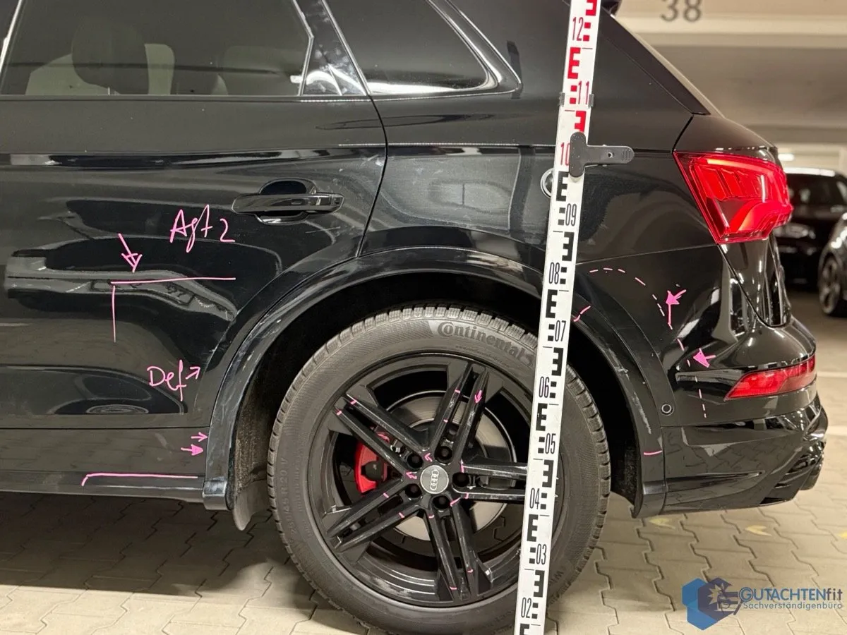 Linke Seite des Audi SQ5 mit markierten Schäden an Tür, Seitenwand und Felge, Messlatte im Bild