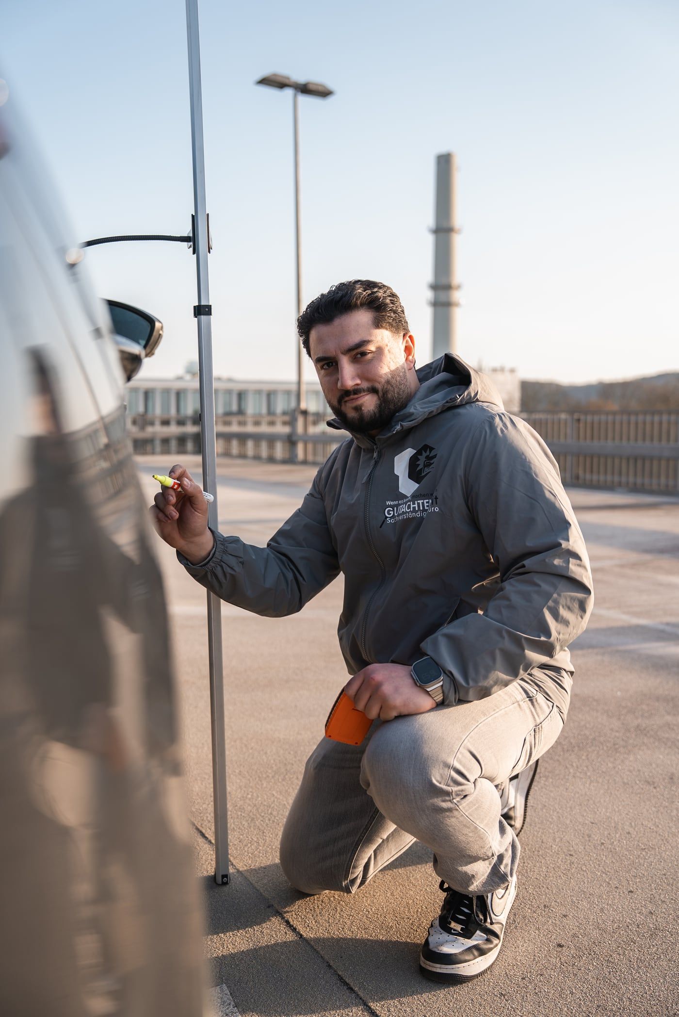Halis Kaya kniet an einer Autotür und markiert einen Schaden