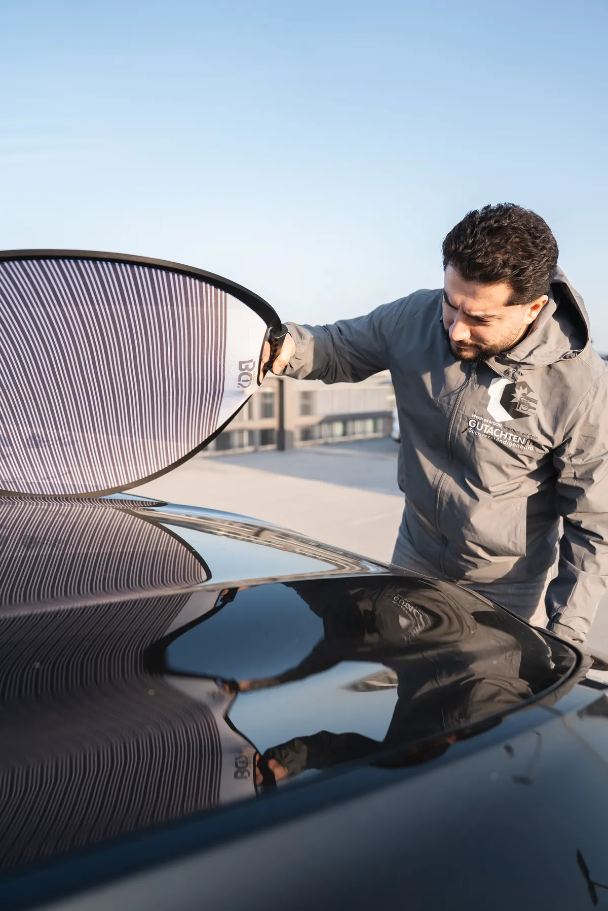 Kfz Gutachter Halis Kaya inspiziert Motorhaube mit Reflektortafel für Unfallgutachten in Bonn